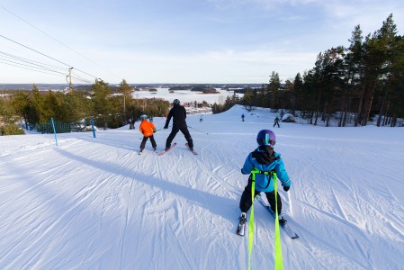 Aloittelevien pikkulaskijoiden kanssa on erilaisia jarruavustusvaihtoehtoja. Kuvassa niistä kaksi suosittua, lasketteluvaljaat ja sauvalla avustaminen